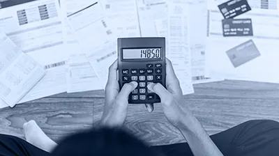 Dirigeant de petite entreprise calculant ses dépenses sur une calculatrice, entouré de factures, illustrant la pression sur les coûts en TPE PME.