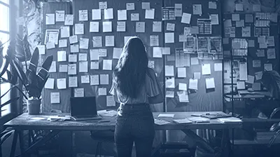 Femme de dos devant un mur couvert de post-it et de documents, illustrant des projets en souffrance faute de pilotage structuré.